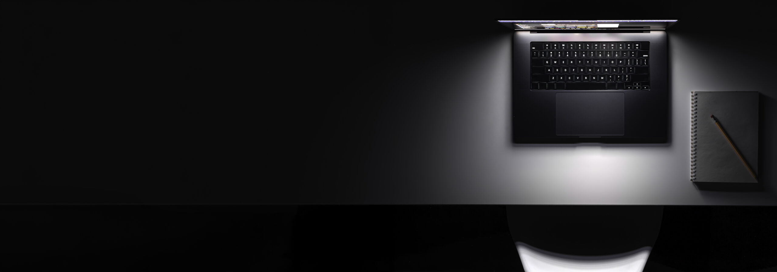 Laptop with a glowing screen on a table in the dark, top view, copy space.